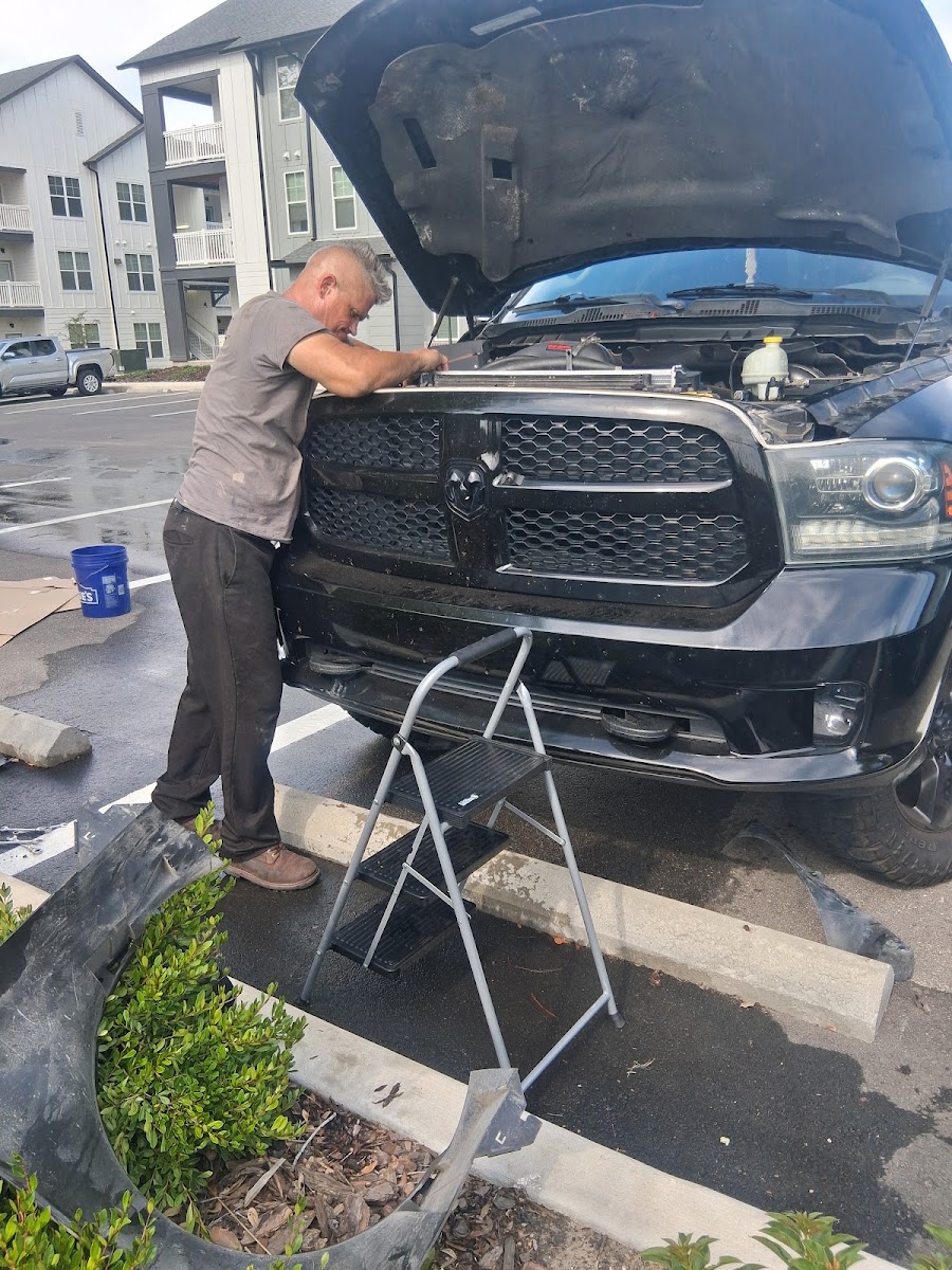 Mechanic working on the front end of a black Dodge Ram truck in a parking lot